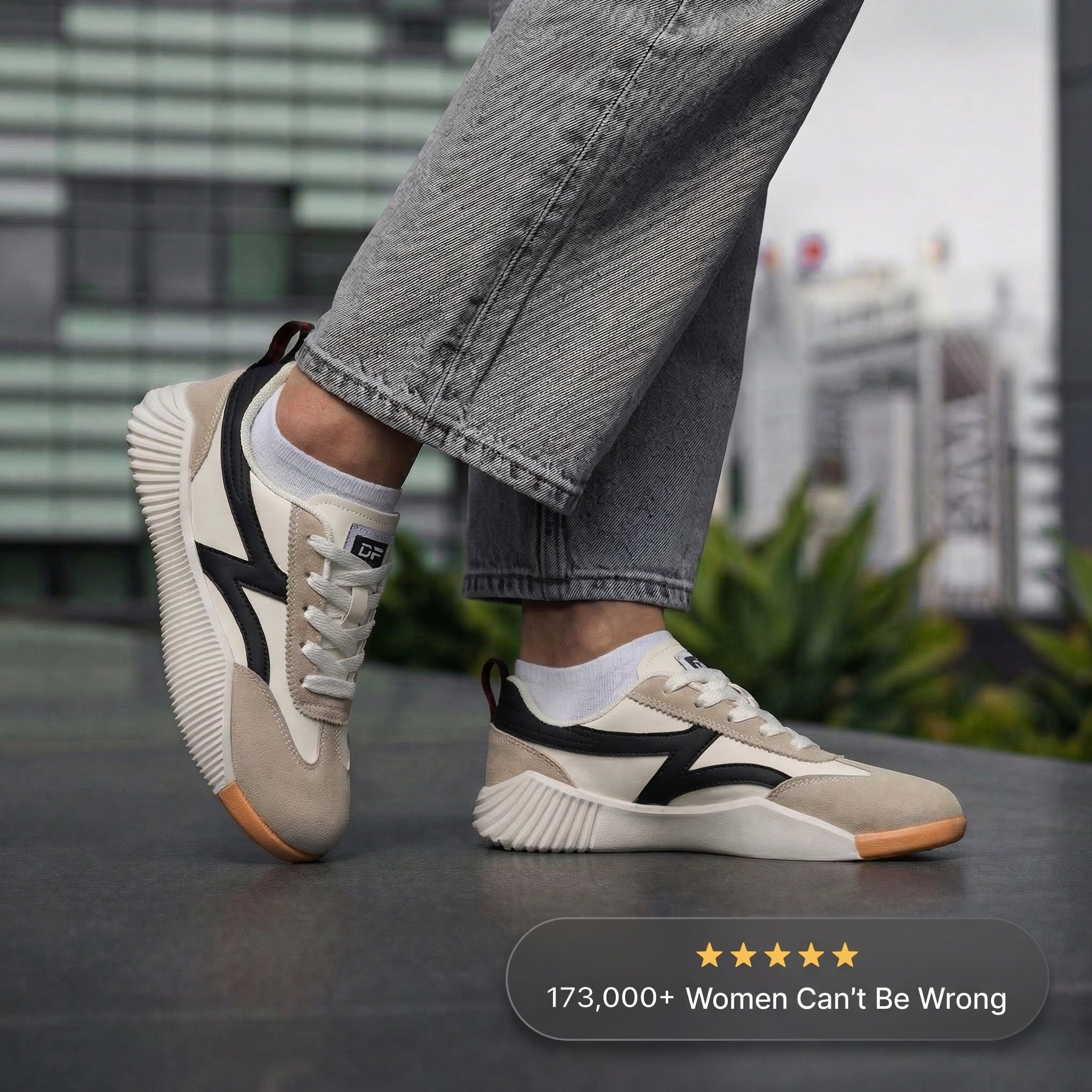 Beige and black sneakers worn with gray jeans on a blurred outdoor background